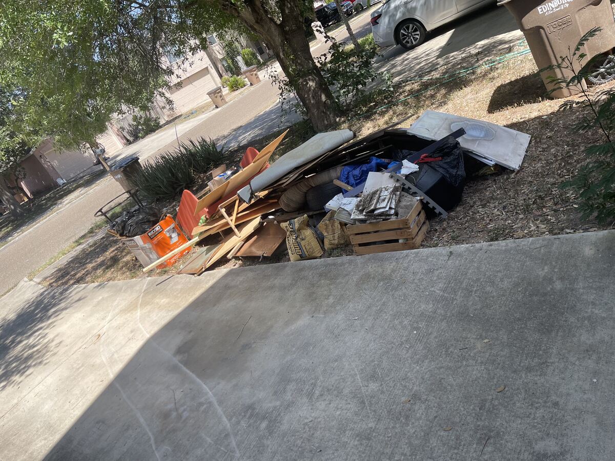 Driveway and garage entrance cluttered with debris before cleanout in San Antonio, TX